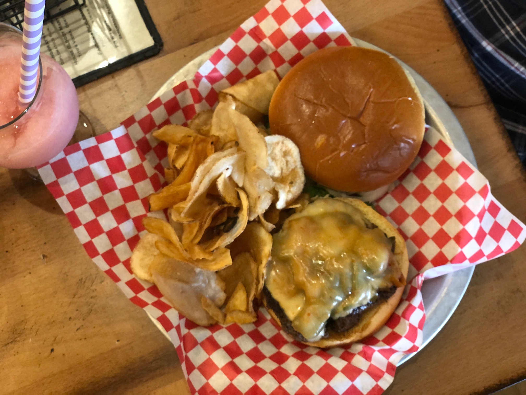 An overhead photo of a burger and fries on a red-and-white checkerboard parchment paper. There is a pink slushie drink with a purple striped straw beside it. Photo by Alyssa Buckley.