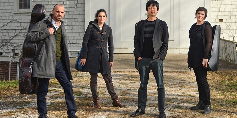 Photo of the members of the Jupiter String Quartet in front of a white shingled building. Photo from KCPA website
