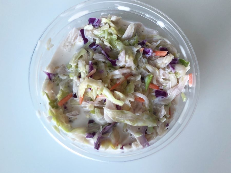 A bowl of coleslaw sits on a white table. The slaw has purple cabbage, carrots, and green cabbage in a white dressing. Photo by Alyssa Buckley.