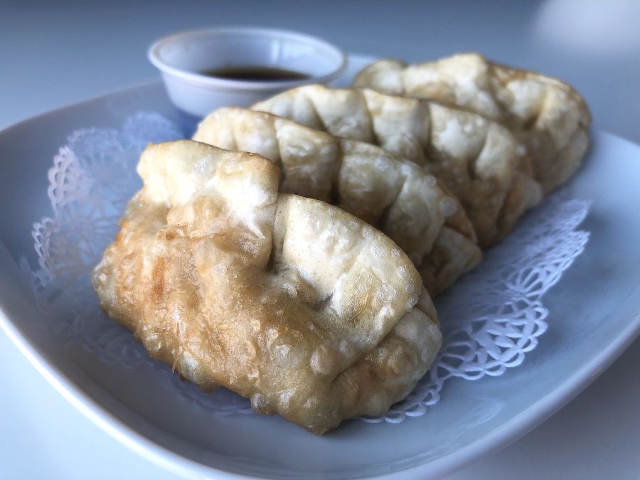 Four pork potstickers sit on a pretty white paper on a white plate. Photo by Alyssa Buckley.