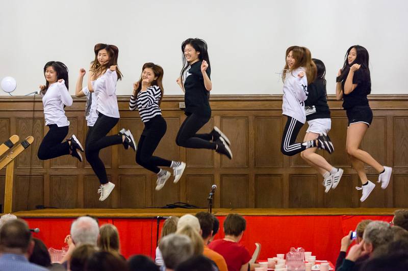 Eight female dancers in black pants, sneakers, and dressy tops jump at the same time on stage at the International Dinner hosted by the UIUC University YMCA in March 2016. Photo by Scott Wells.