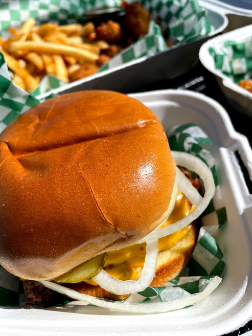An all American burger with fries sits in a takeout container lined with a green and white checkered paper. Photo by Remington Rock.