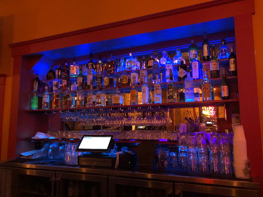 The inside of Cowboy Monkey showcases many bottles of liquor at the back of the bar. There is a computer for ringing orders in the center below. Photo by Alyssa Buckley.