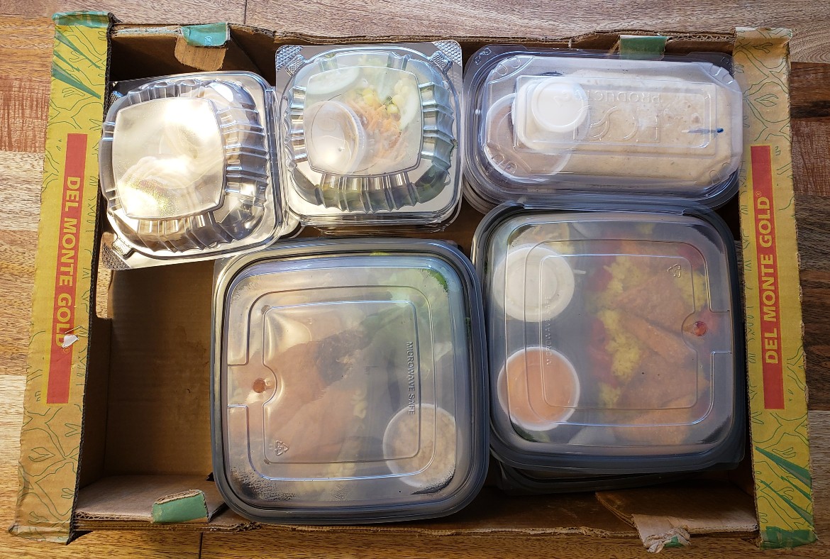 An overhead shot of several takeout containers filled with food in a reused paper box. Photo by Sara Ressing.