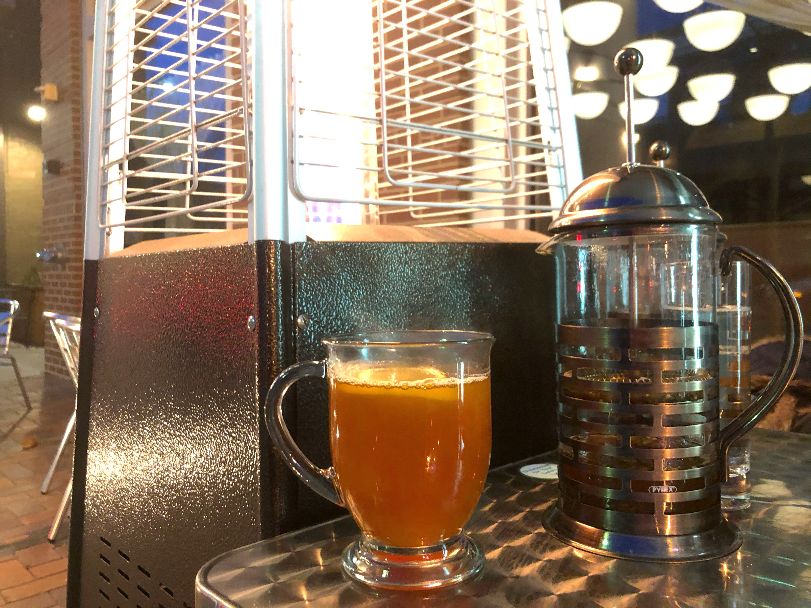 A full glass of hot toddy sits besides a French press on a silver outdoor table at Punch!. Photo by Alyssa Buckley.