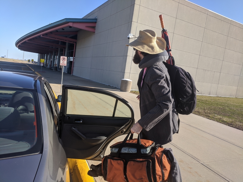 The writer is standing by an open car door at the entrance to Willard Airport. He has a duffle bag and a backpack. Photo by Andrea Black.
