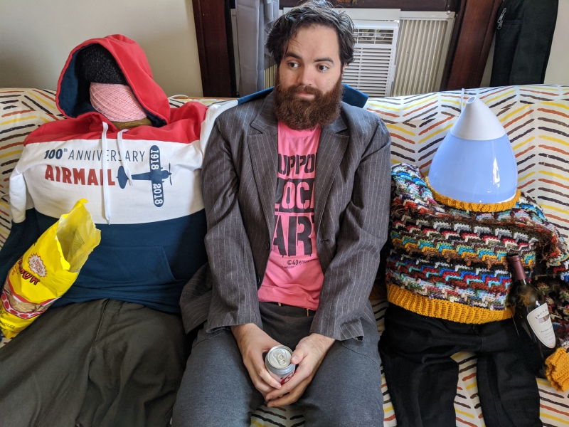 The writer is sitting on a couch in between two fake people fashioned out of clothing and other household items. Photo by Andrea Black.