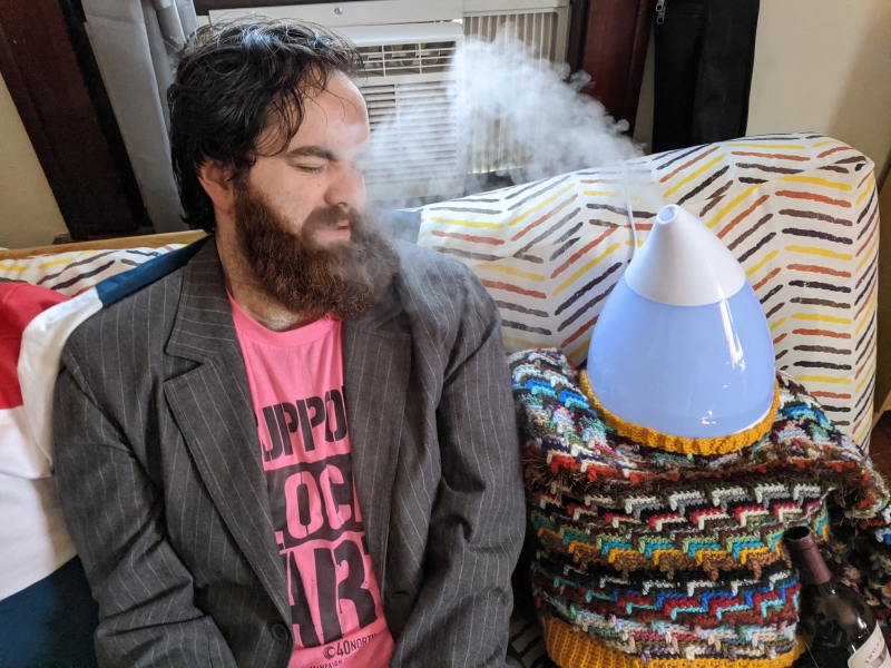 The writer is turned toward a fake person with a humidifier as the head, and is breathing in the water droplets from the humidifer. Photo by Andrea Black.