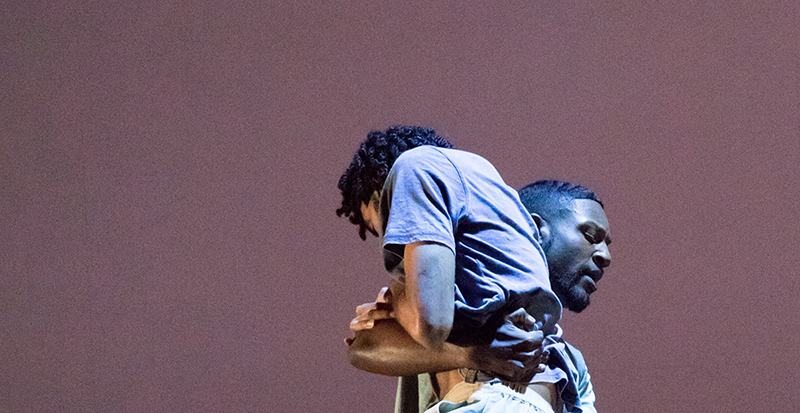 Two black male dancers entwined on stage. Photo from the Dance at Illinois Facebook page.