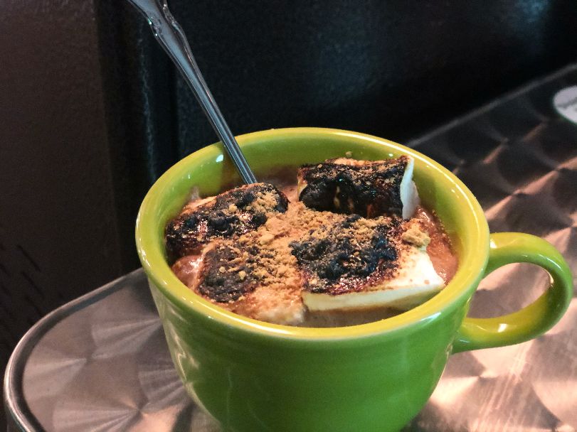 A green mug holds a cocktail with charred marshmallows and a metal fork sticking out. Photo by Alyssa Buckley.