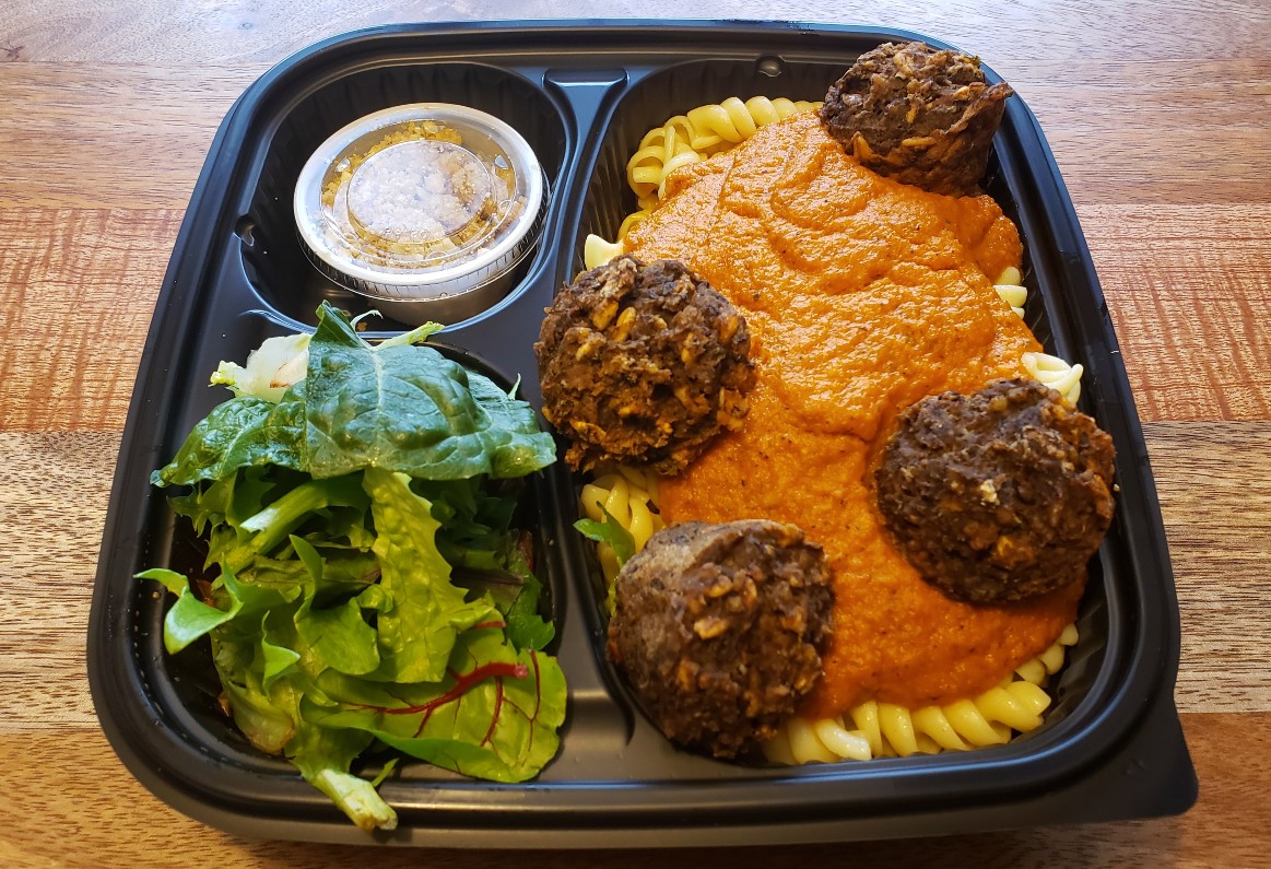 A takeout meal from Red Herring includes a side salad, a cup of dressing, and a large portion of rotini noodles with mushroom 