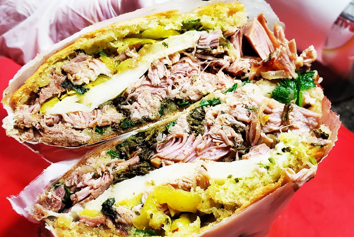  view of two halves of Baldarottaâ€™s Porketta sandwich shows layers of shredded pork, chunky salsa verde, and sliced banana peppers with a thick layer of provolone cheese running through the center of the other ingredients. Photo by Jordan Baldarotta.
