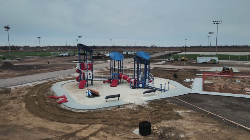 A blue and red play structure on a concrete slab. It is surrounded by dirt. Photo by Cole Carpenter.