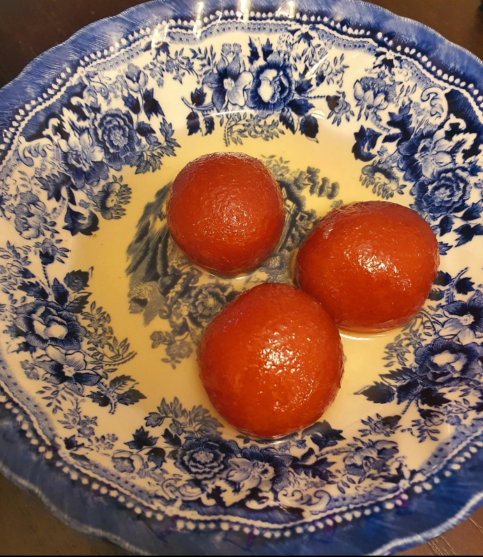 Three balls of gulab jamun sit in a beautiful white and blue floral plate in a pool of syrup. Photo by Da Yeon Eom.