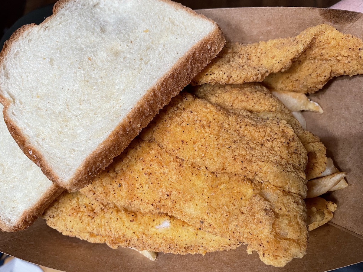 Fried fish fillets from Wood N' Hog sit atop fries with a white slice of bread on top. Photo by Anthony Erlinger.