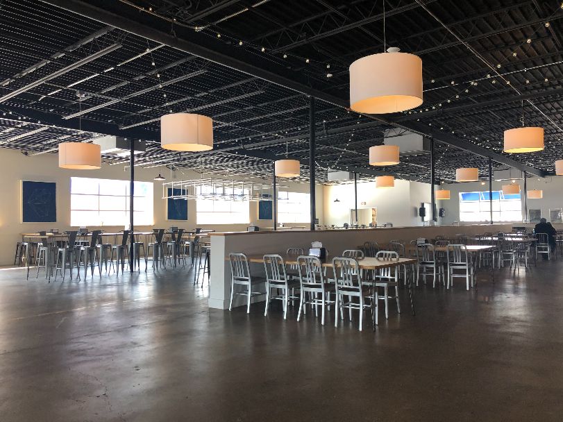 The interior of Broadway Food Hall with many tables, empty and distanced, with overhead circle fabric lights and string lights under the black industrial high ceiling. Photo by Alyssa Buckley.
