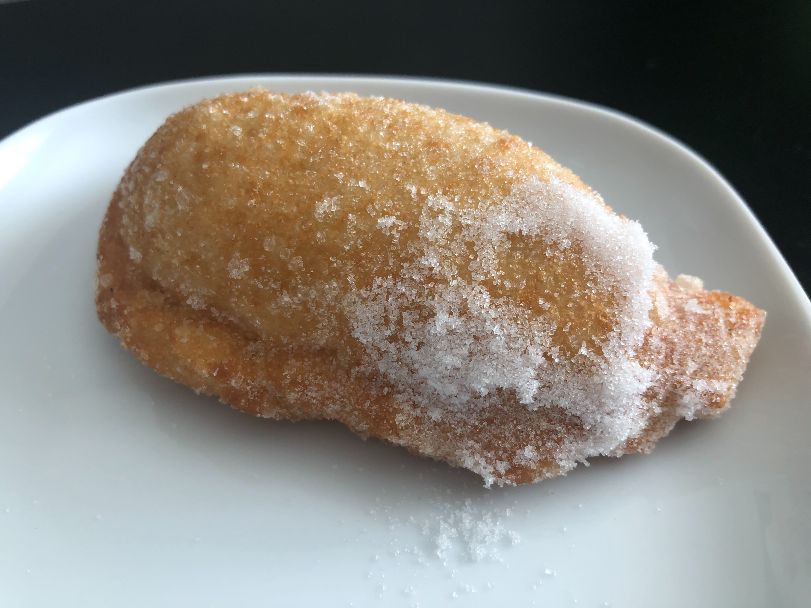 A dessert empanada dusted with grains of white sugar sits on a white plate on a black table. Photo by Alyssa Buckley.