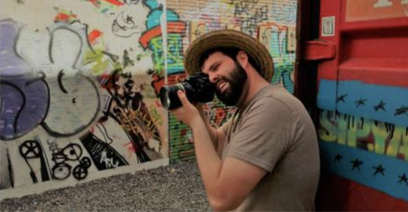 Photo of Sam Logan holding a camera to his eye at Sipyard. Photo by Sal Nudo.