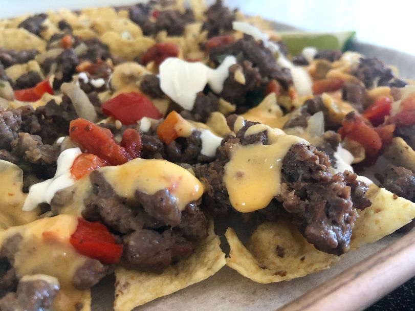 Homemade nachos by the author have cooked taco beef mix with cooked veggies, red salsa, yellow melted queso, and dollops of sour cream over tortilla chips. Photo by Alyssa Buckley.