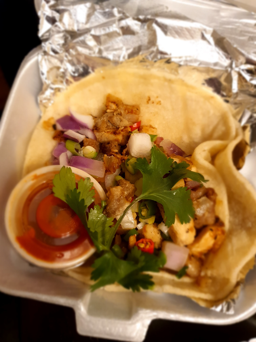 A sisig taco sits on tin foil in a takeout container. Photo by Da Yeon Eom.