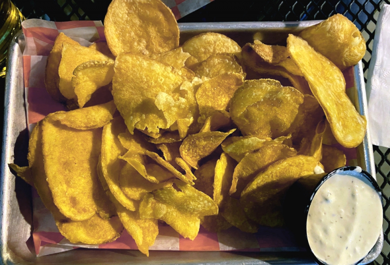 A metal tray is lined with red and white checked wax paper. It is filled with fresh cut potato chips, and a small plastic cup filled with white sauce. Photo by Julie McClure.