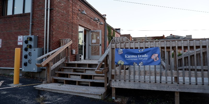 A wooden deck with stairs leading up to a large platform. It is behind a red brick building. A blue sign that says Karma Trade hangs on the side of the deck. Photo provided by Karma Trade.