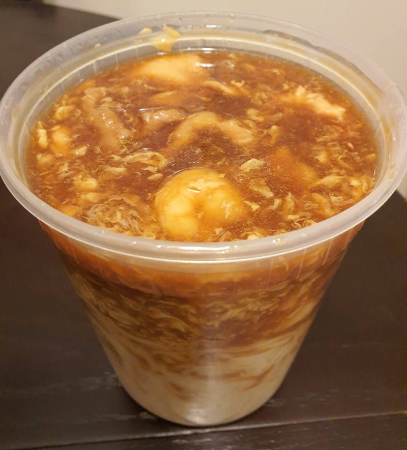 A soup from Lai Lai Wok sits in a plastic, cylindrical container from Lai Lai Wok. There are floating chunks of meat and veggies. Photo by Da Yeon Eom.