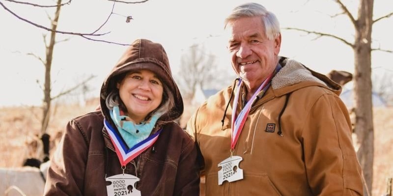 Prairie Fruit Farms and Creamery owners Leslie Cooperband and Wes Jarrell standing outside in coats wearing their Good Food Awards 2021 medals. Photo courtesy of Prairie Fruit Farms and Creamery
