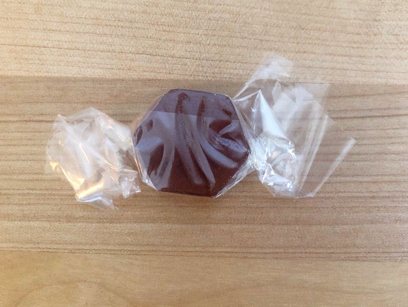 On a wooden counter, a purple-brown lozenge sits, wrapped in clear packaging like a candy. Photo by Alyssa Buckley.