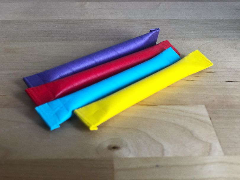 Four pixie straws in yellow, blue, red, and purple sit on a butcher block counter. Photo by Alyssa Buckley.