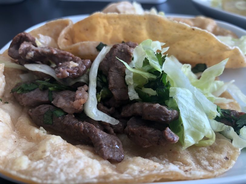 A close up photo of the steak taco from El Paraiso with long, charred strips of steak with lettuce on a doubled corn tortilla. Photo by Alyssa Buckley.
