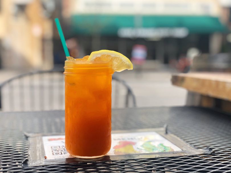 On a black outdoor table, there is a glass cup with an orange drink and a wedge of lemon with a green straw. On the table is a taped image of a chicken and a QR code for the menu at Watson's Shack & Rail. Photo by Alyssa Buckley.