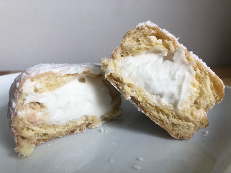 A white cream filled powdered donut is cut in half showing the white cream center. The donut is on a white square plate. Photo by Alyssa Buckley.