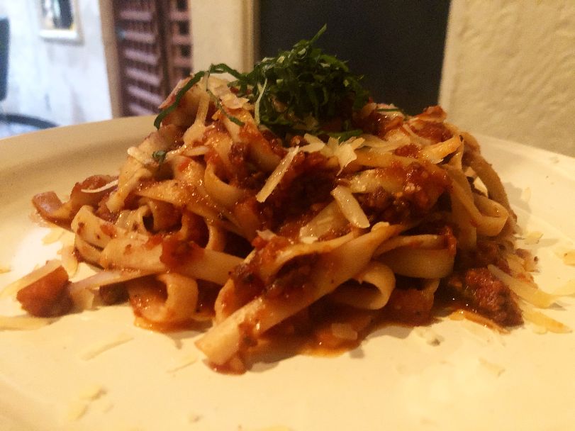 On a beige plate, there is a pile of fettuccine noodles with a light bolognese sauce topped with thin ribbons of basil and grated cheese. Photo by Alyssa Buckley.