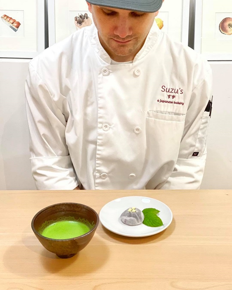 Chef Alex Sentowski with a bowl of freshly whisked matcha tea and a mochi sweet sitting on a plate with decorate leaves next to the mochi. Photo by Suzu's Bakery.