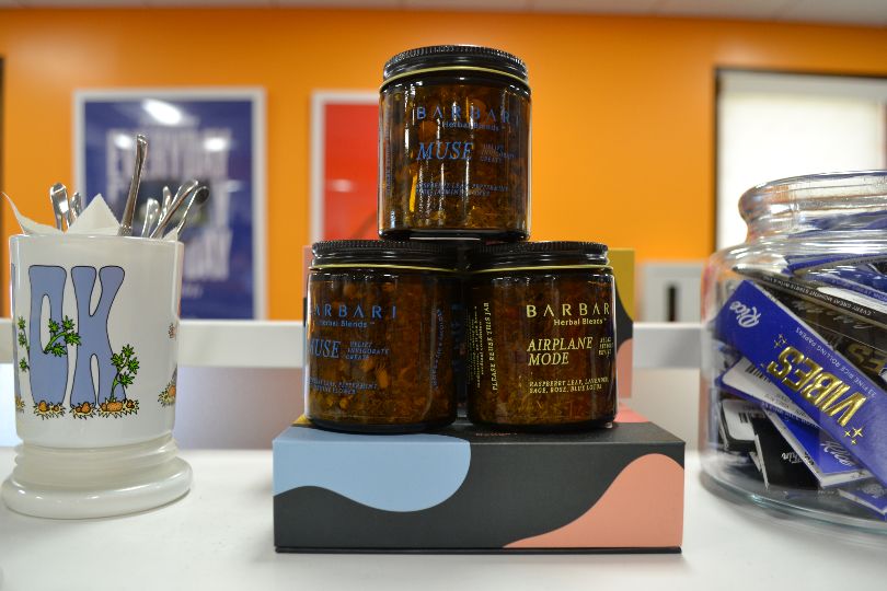 Three brown glass jars are stacked in a miniature pyramid on a counter in Sunnyside Champaign. The background wall is orange with blurred posters. Photo by Alyssa Buckley.
