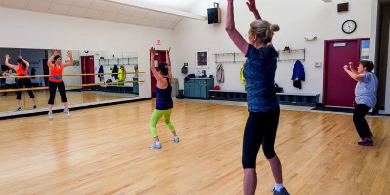 Four women are exercising in a studio with a wood floor and wall of mirrors. Photo from Urbana Parks Foundation website.