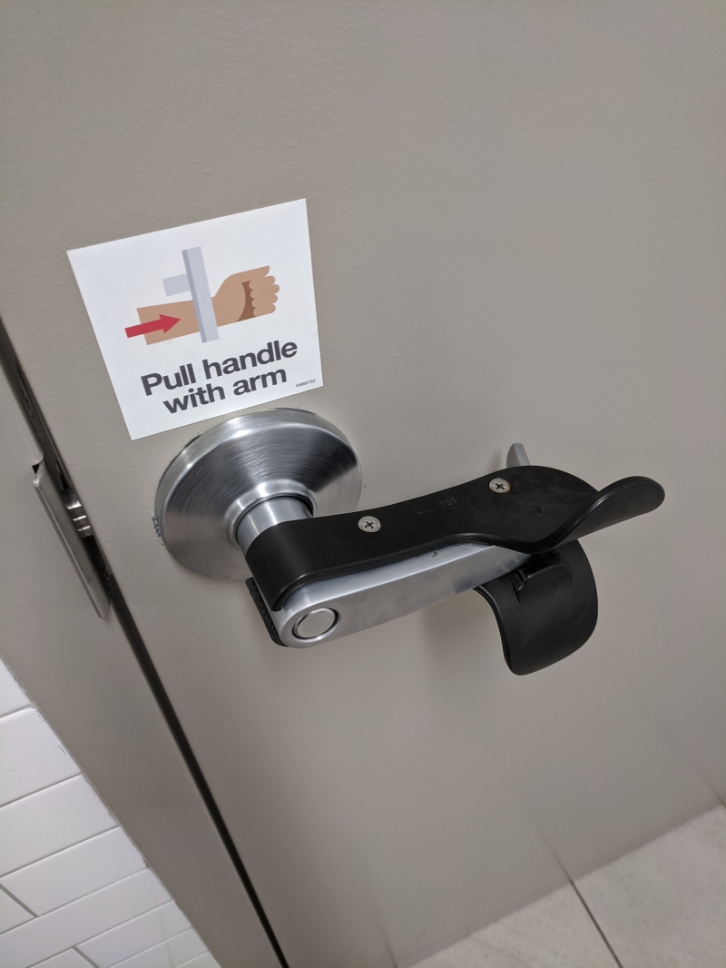 A metal door handle has a black plastic implement attached to it. A sign that says 