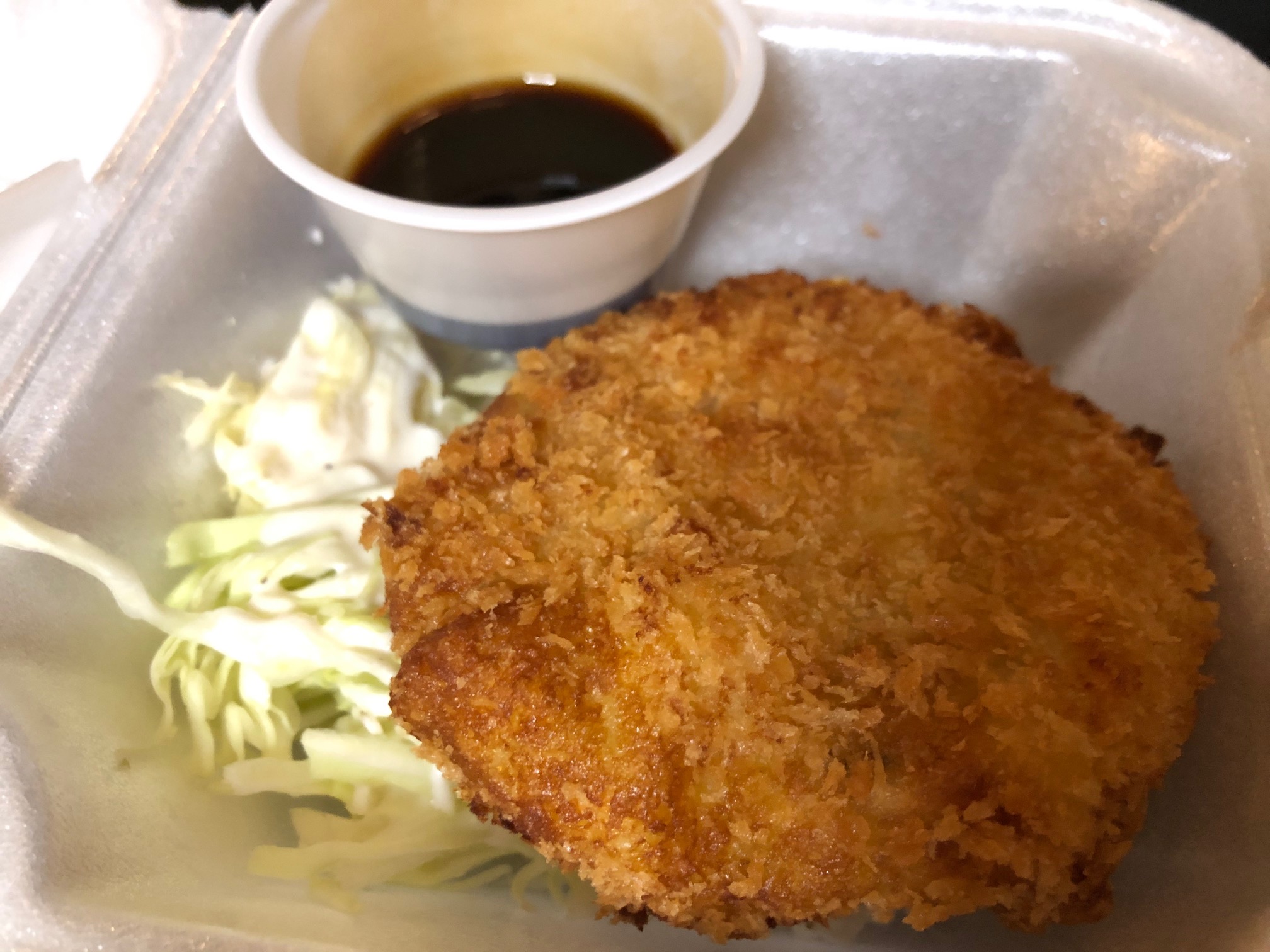 There is a korokke appetizer in a small square takeout container. There is also undressed lettuce and a cup of dipping sauce. Photo by Alyssa Buckley.