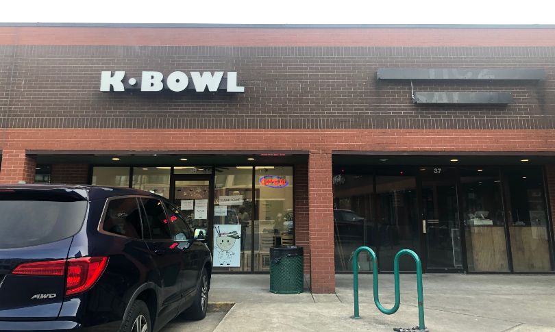 The exterior of the restaurant which reads K Bowl on a brick building in front of a parking lot. Photo by Alyssa Buckley.