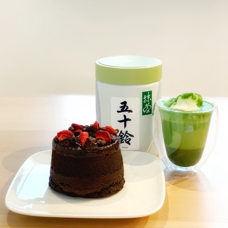 A circular piece of okara cake, a large canister of matcha powder, and a multilayered matcha latte artfully displayed. Photo by Suzu's Bakery.