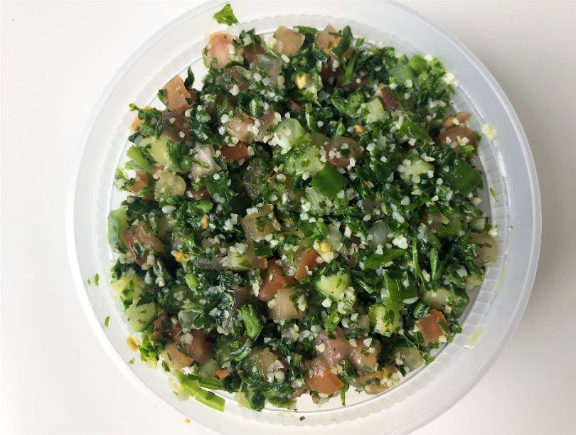 An overhead photo of a circular takeout container of tabouli salad shows finely chopped herbs and diced tomatoes. Photo by Alyssa Buckley.
