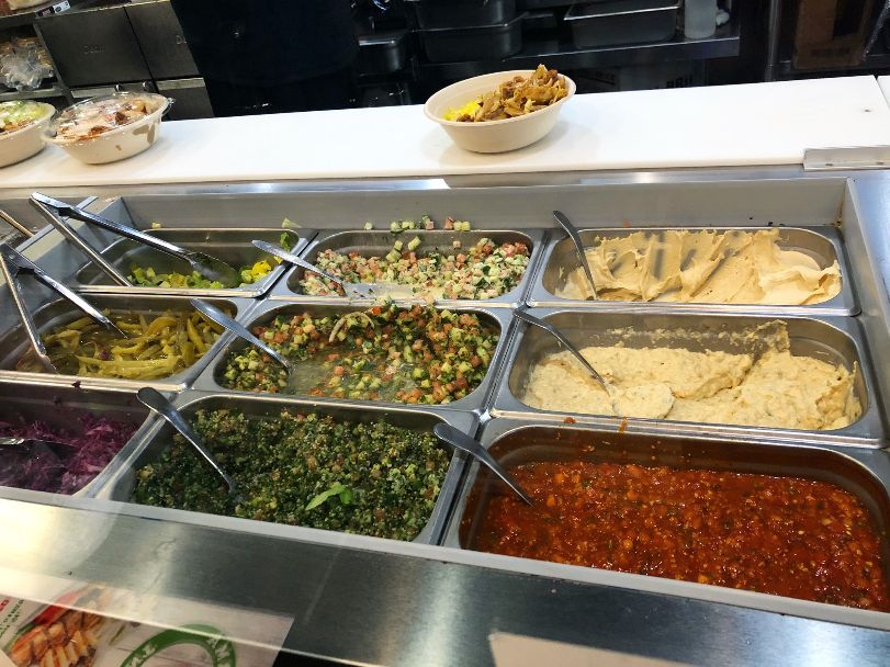 There are nine metal containers on a line holding toppings for pitas and bowls at Shawarma Joint. Photo by Alyssa Buckley.