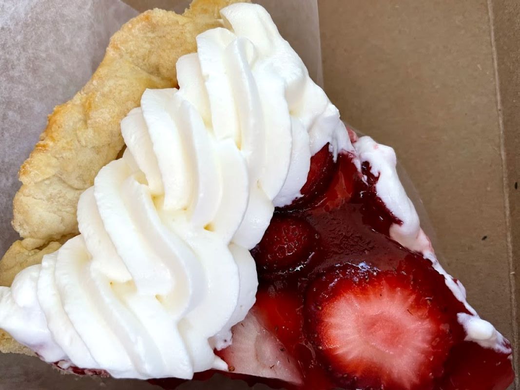 A triangular slice of strawberry pie sits in a brown paper box with parchment paper. Photo by Remington Rock.