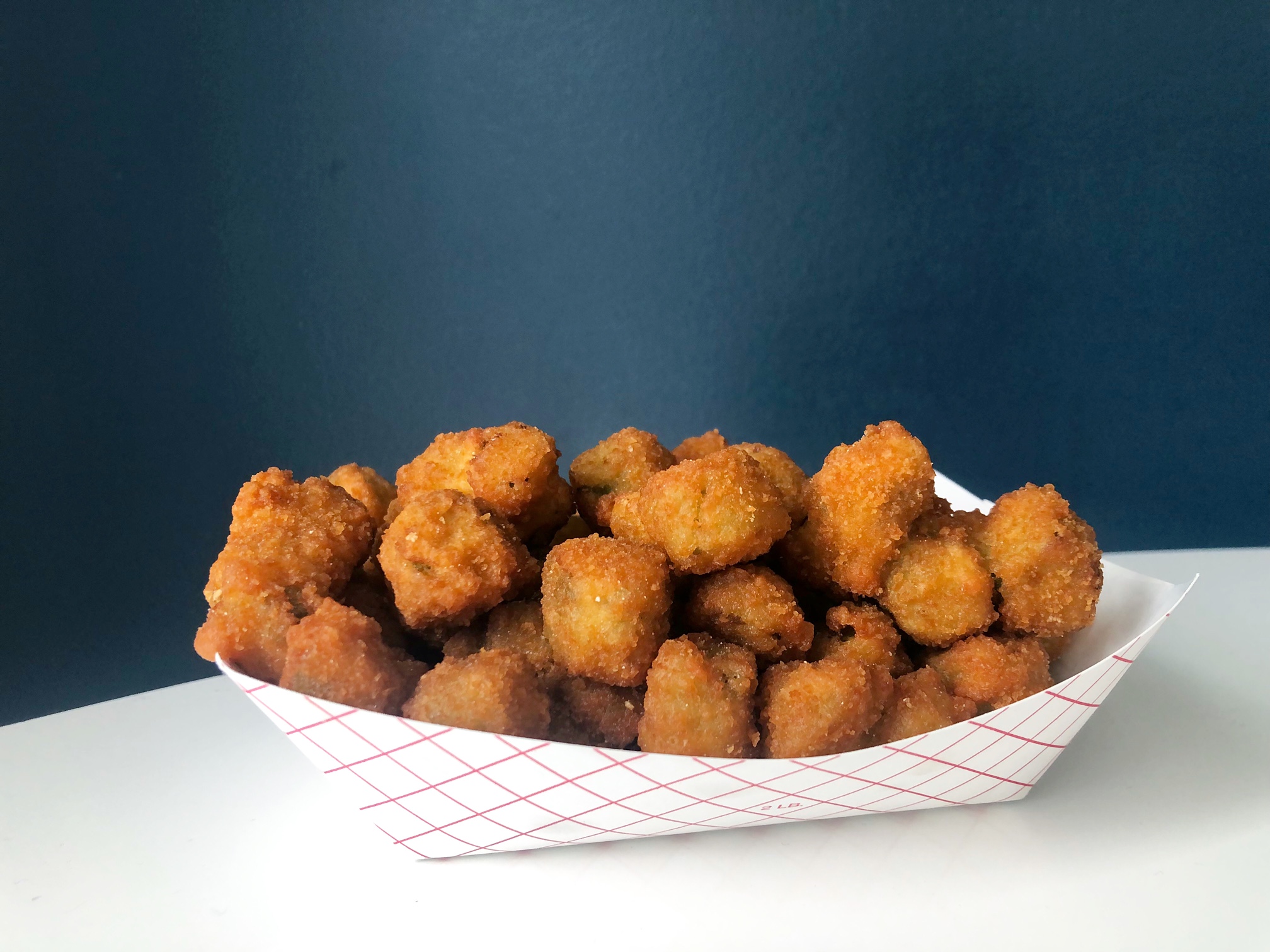A paper basket of fried okra sits on a white table in front of a blue wall. Photo by Alyssa Buckley.