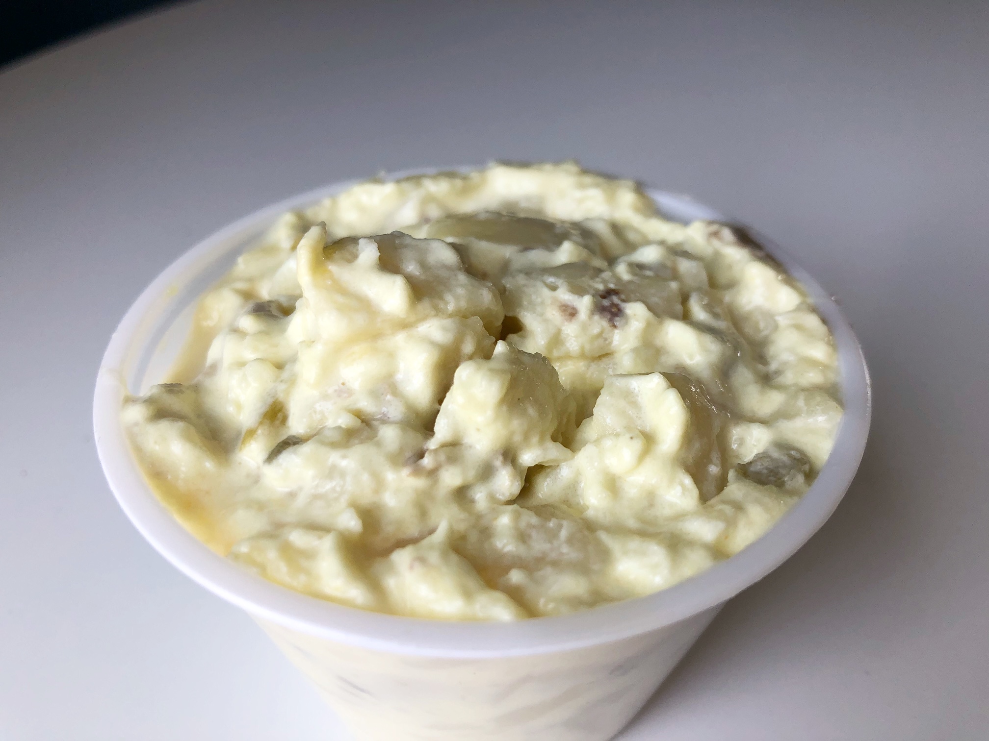 On a white table, there is a small side cup of yellow potato salad. Photo by Alyssa Buckley.