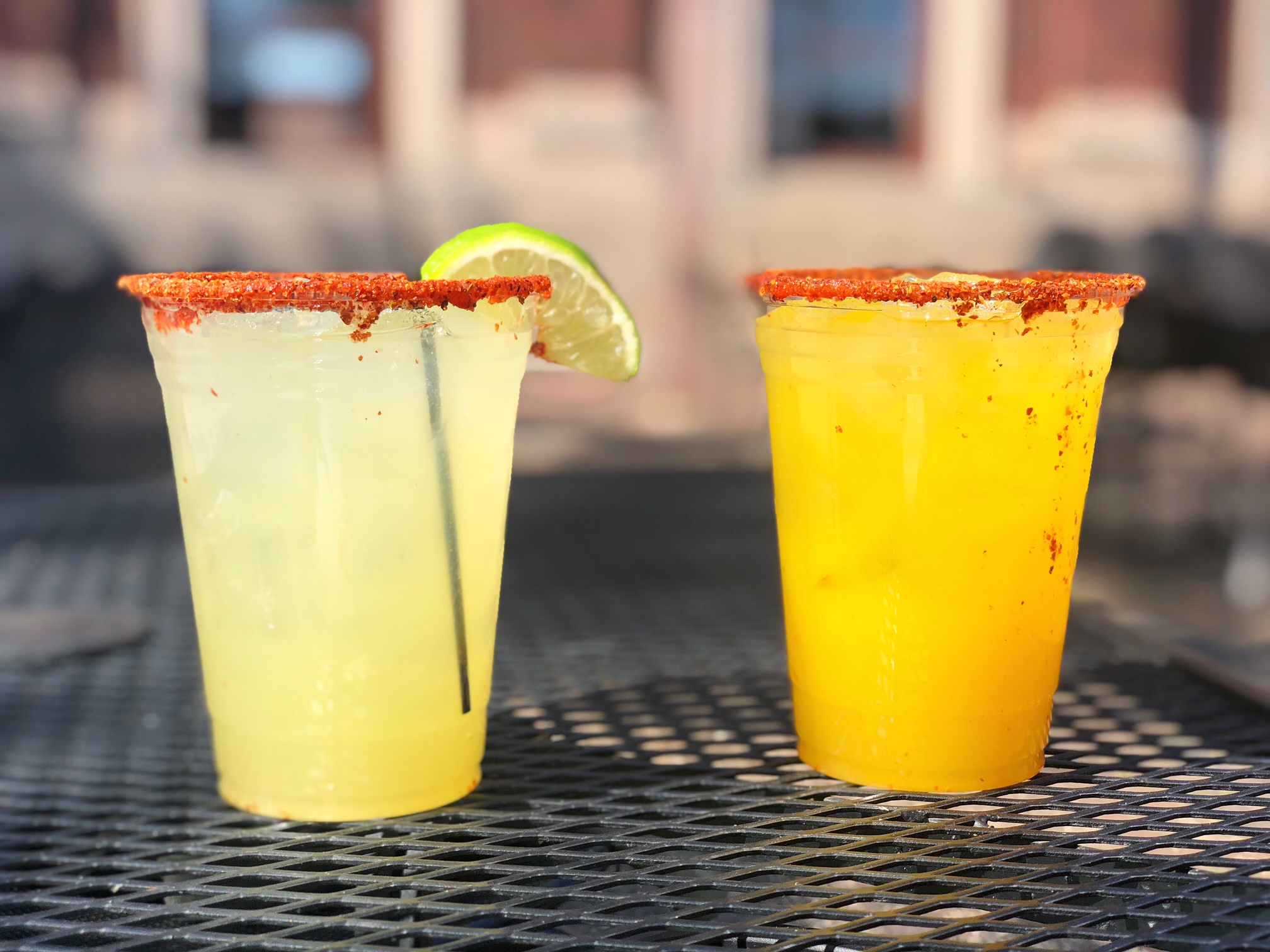 Two margaritas from Maize sit on the black metal outdoor patio table. The one on the left is light green, and the one on the right is orange. Photo by Alyssa Buckley.