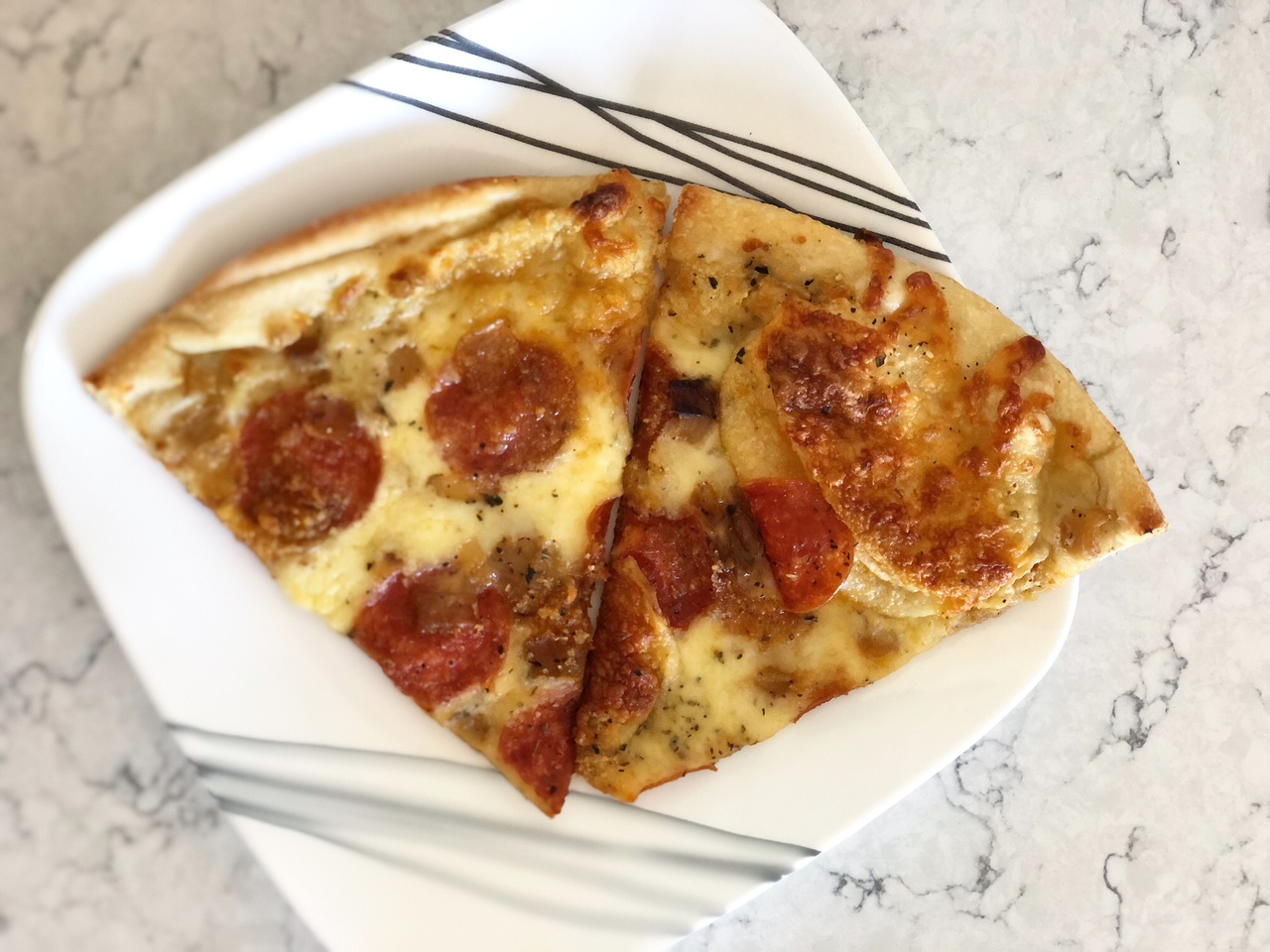 Two slices of pizza are on a white plate on a marbled counter. Photo by Alyssa Buckley.