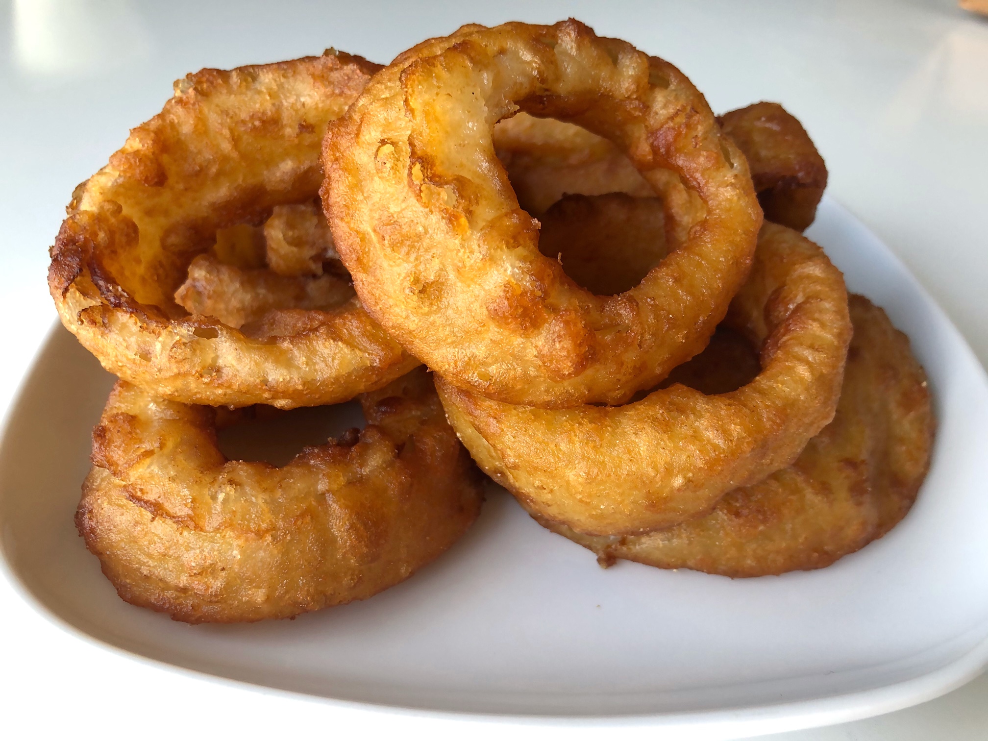 On a white plate, there are several golden brown onion rings. Photo by Alyssa Buckley.