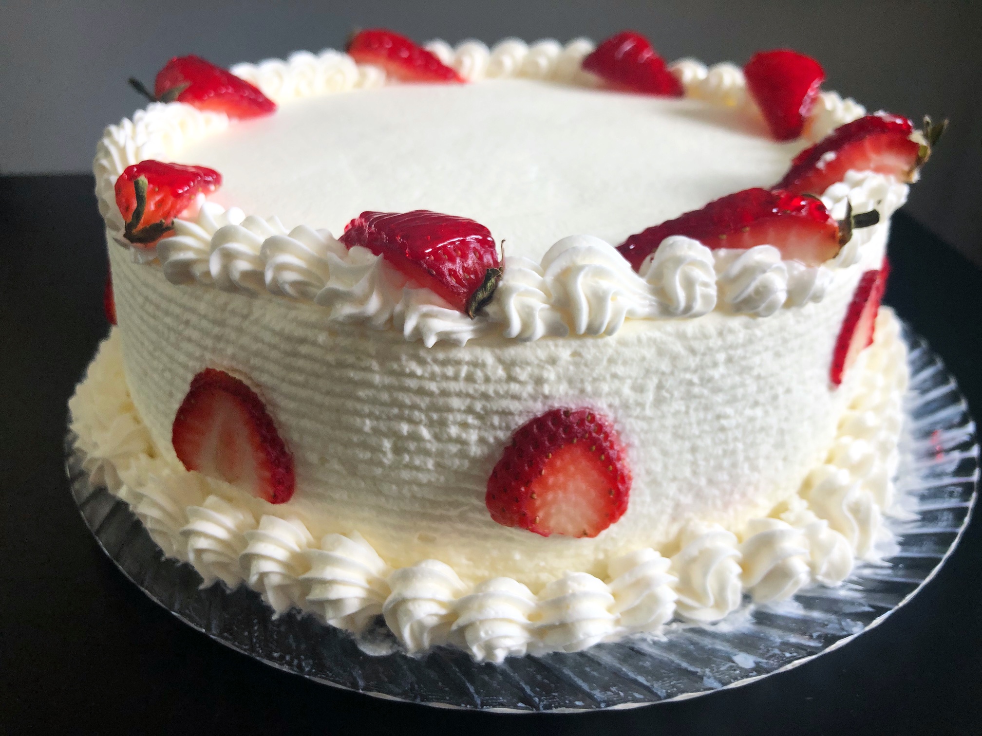 On a black table, there is a large white cake with sliced strawberries as garnish. Photo by Alyssa Buckley.